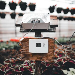 Thermostat and sensor controlling climate inside a greenhouse filled with plants.